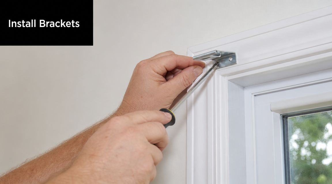 A person uses a screwdriver to attach a metal blind mounting bracket to the window frame.