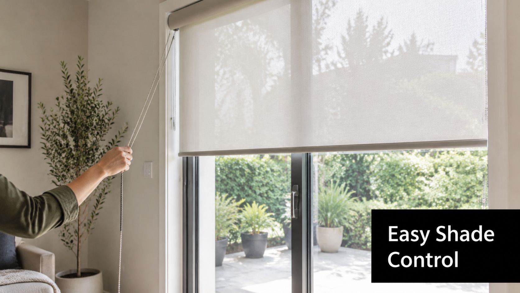 A person uses a beaded chain to lower a sheer roller shade over a large sliding glass door.